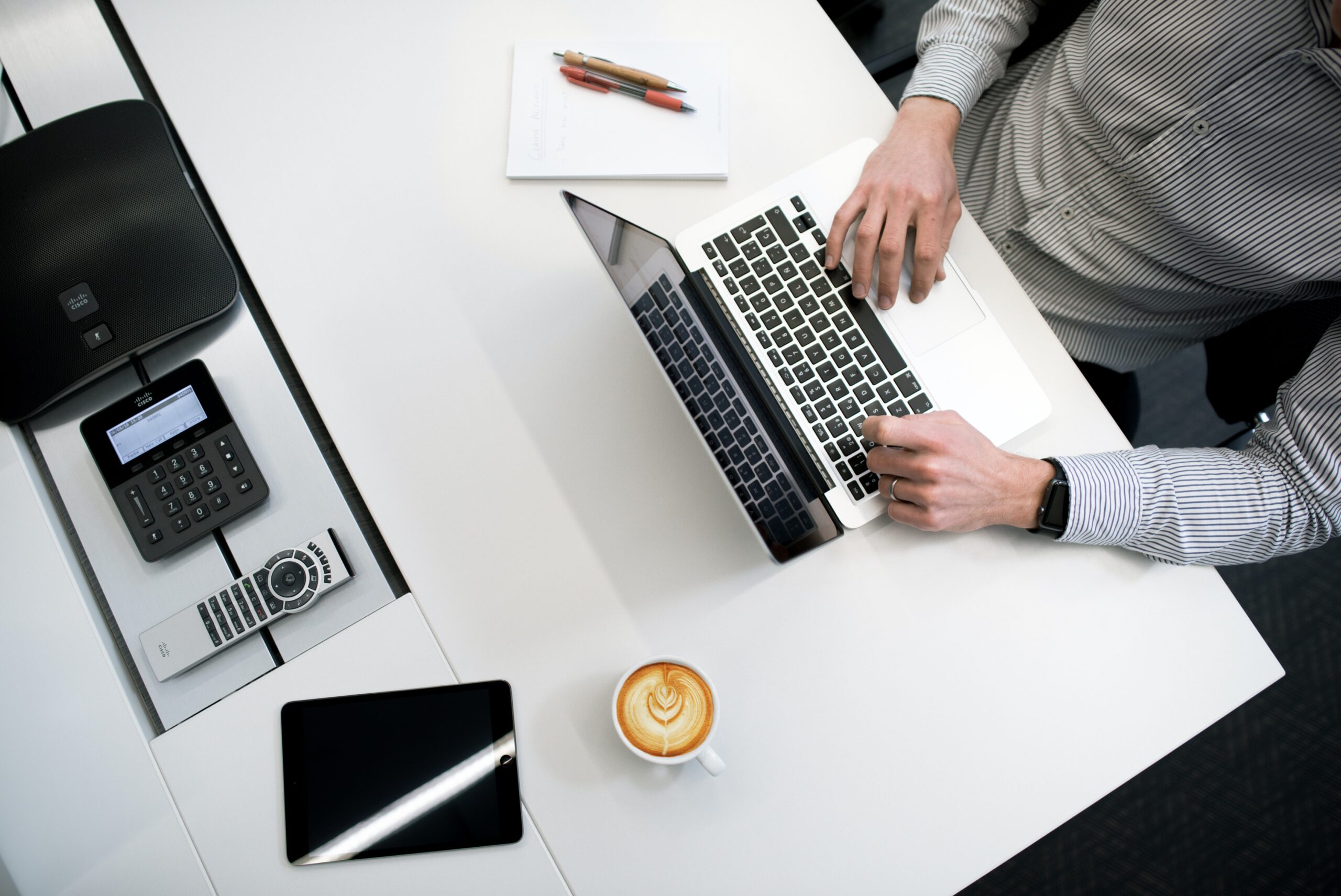 Desk with coffee, tablet and someone working at a laptop